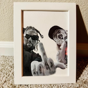 May include: A framed monochrome painting featuring two figures. One figure wears sunglasses, the other a hat. A hand with an extended middle finger is central. The artwork is presented within a white frame, suitable for wall display.