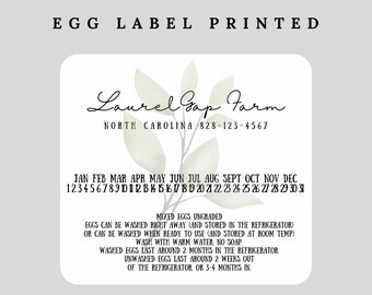 May include: A white label with green watercolor leaves and the text "Laurel Gap Farm" in black cursive font. Below the farm name is the text "NORTH CAROLINA 828-123-4567". Below that is a calendar with the months of the year and the numbers 1 through 31. Below the calendar is text about how to store eggs, including information about washing and storage times.