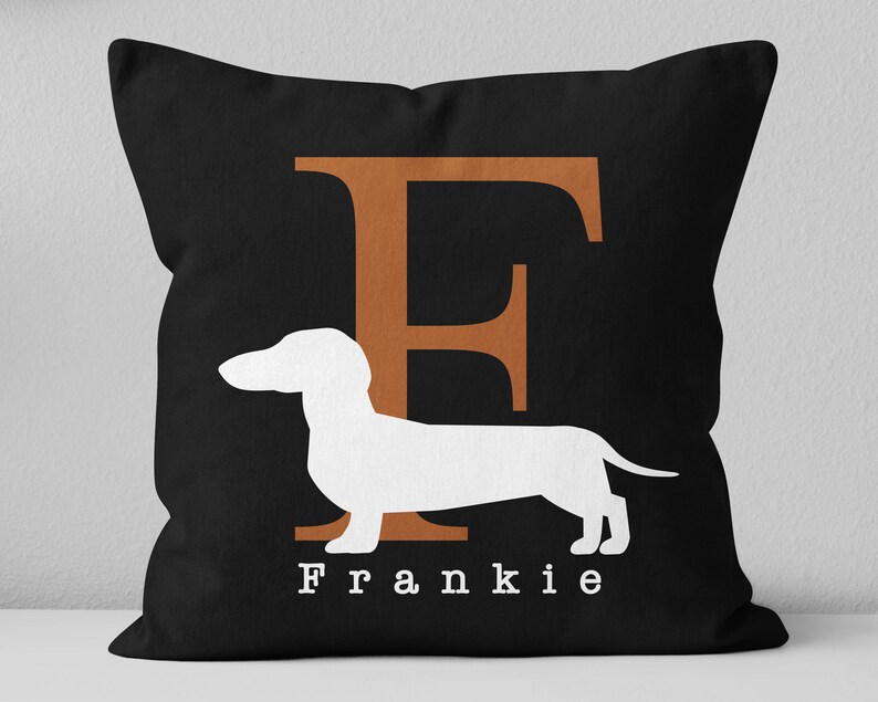 May include: Black throw pillow with a white dachshund silhouette and the letter "F" in orange. The text "Frankie" is printed below the dachshund.