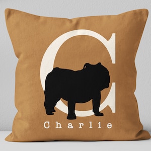 May include: A brown throw pillow with a white letter C and a black silhouette of a bulldog. The pillow has the name "Charlie" printed in white letters.