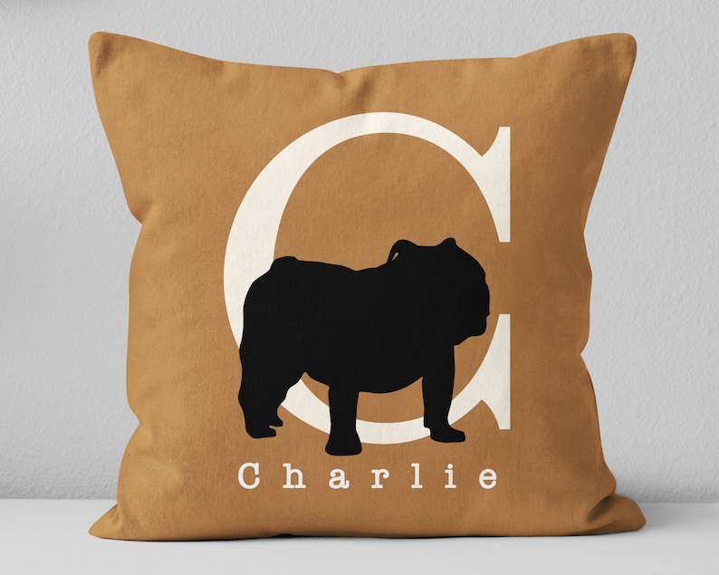 May include: A brown throw pillow with a white letter C and a black silhouette of a bulldog. The pillow has the name "Charlie" printed in white letters.