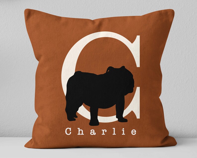 May include: A brown throw pillow with a white letter C and a black silhouette of a bulldog. The pillow has the name "Charlie" printed in white letters.
