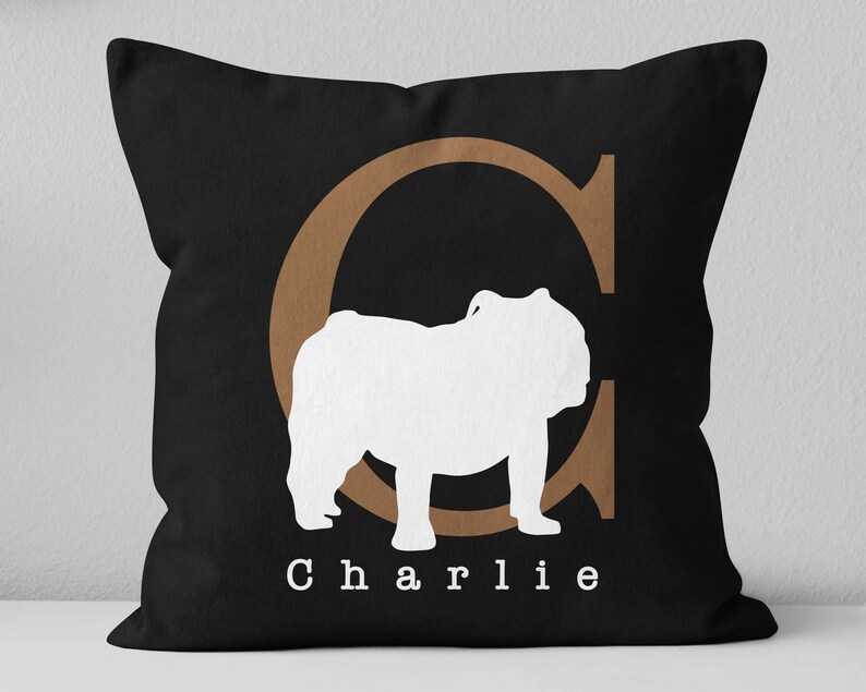 May include: Black pillow with a brown letter C and a white silhouette of a bulldog. The pillow has the name "Charlie" printed on it.