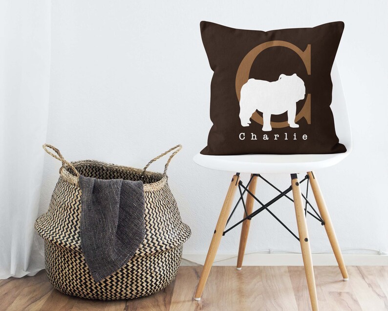 May include: A brown throw pillow with a white silhouette of a bulldog and the letter "C" in a brown font. The pillow has the name "Charlie" printed in white below the bulldog.