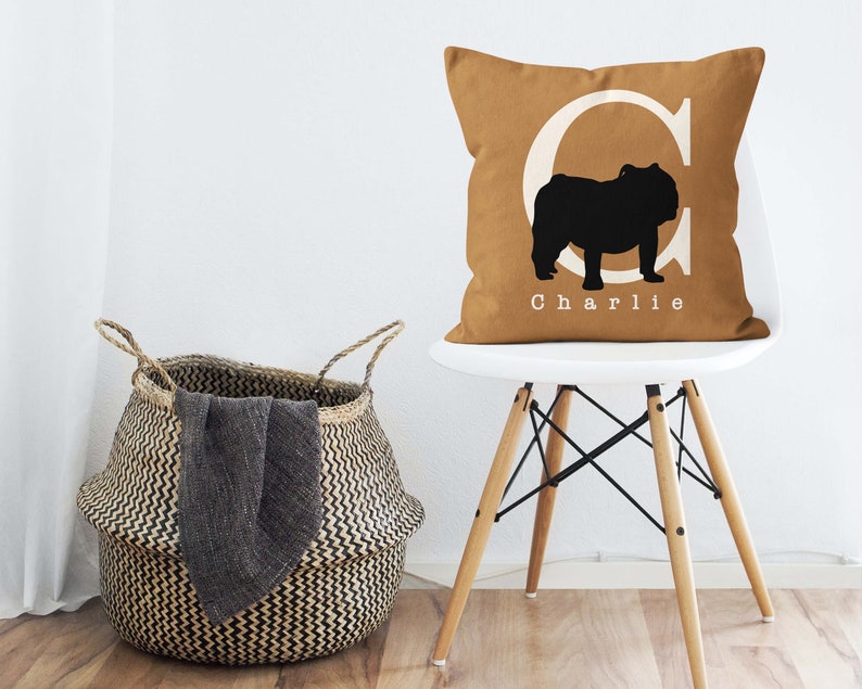 May include: A brown throw pillow with a white letter C and a black silhouette of a bulldog. The pillow has the name "Charlie" printed in white below the bulldog.