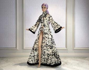 May include: A doll wearing a long, white and black patterned coat with a black trim. The coat is open in the front, revealing the doll's legs. The doll has purple hair and is standing on a white tiled floor.