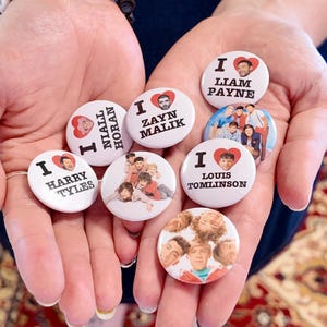 Puede incluir: Una colección de chapas redondas con los miembros de One Direction. Cuatro chapas muestran un corazón rojo con el texto I love seguido del nombre de Harry Styles, Niall Horan, Zayn Malik, Liam Payne o Louis Tomlinson. Dos chapas muestran fotos de grupo.