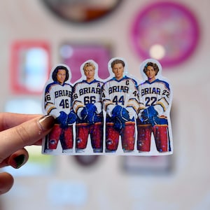Pode incluir: Um adesivo hologr&aacute;fico com quatro jogadores de h&oacute;quei lado a lado. Cada jogador veste uma camisa branca com detalhes em azul e amarelo, a palavra BRIAR e os n&uacute;meros 46, 66, 44 e 22. Eles usam luvas azuis e cal&ccedil;&otilde;es vermelhos.