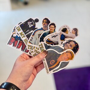 Pode incluir: Uma cole&ccedil;&atilde;o de autocolantes hologr&aacute;ficos com v&aacute;rias imagens de pessoas, camisolas desportivas com o n&uacute;mero 44 e texto incluindo "IN MY HO", "TEAM", "baby, now that I found you, I can't let you go" e "LAURENTIS" com um acabamento brilhante.