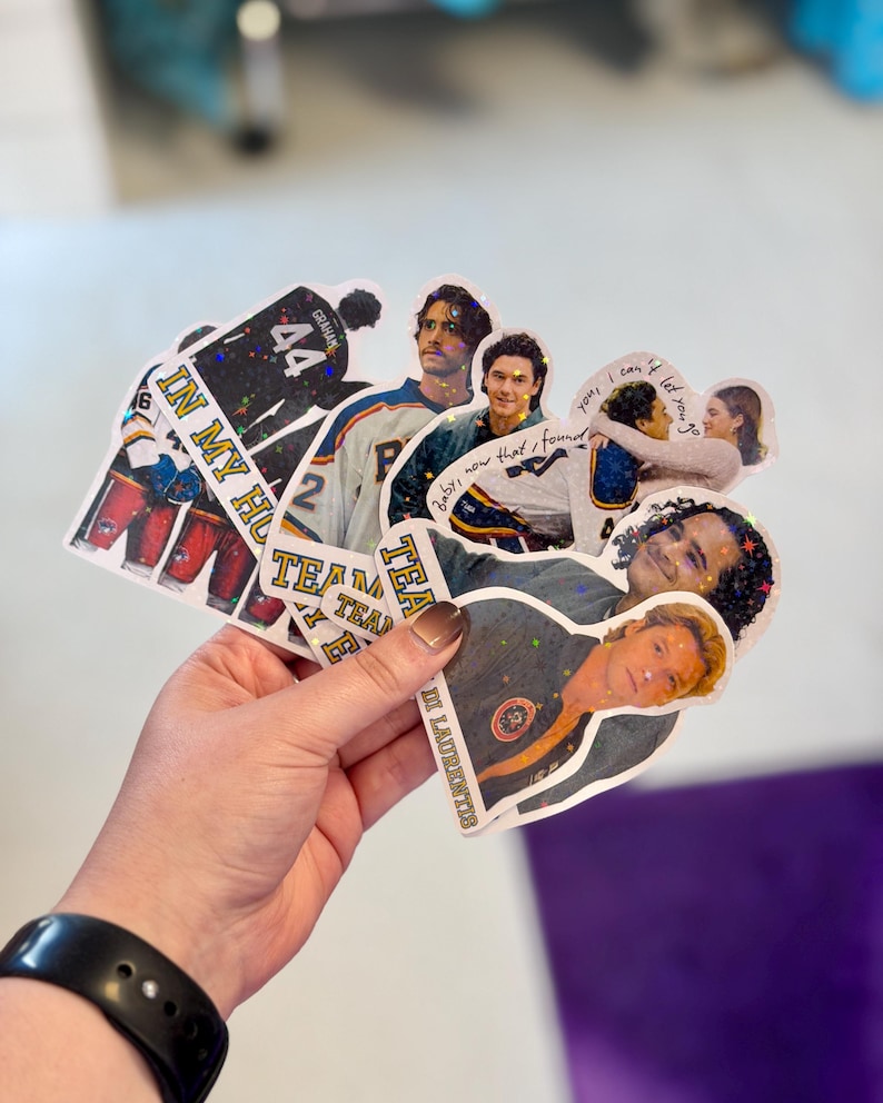 Pode incluir: Uma cole&ccedil;&atilde;o de autocolantes hologr&aacute;ficos com v&aacute;rias imagens de pessoas, camisolas desportivas com o n&uacute;mero 44 e texto incluindo "IN MY HO", "TEAM", "baby, now that I found you, I can't let you go" e "LAURENTIS" com um acabamento brilhante.