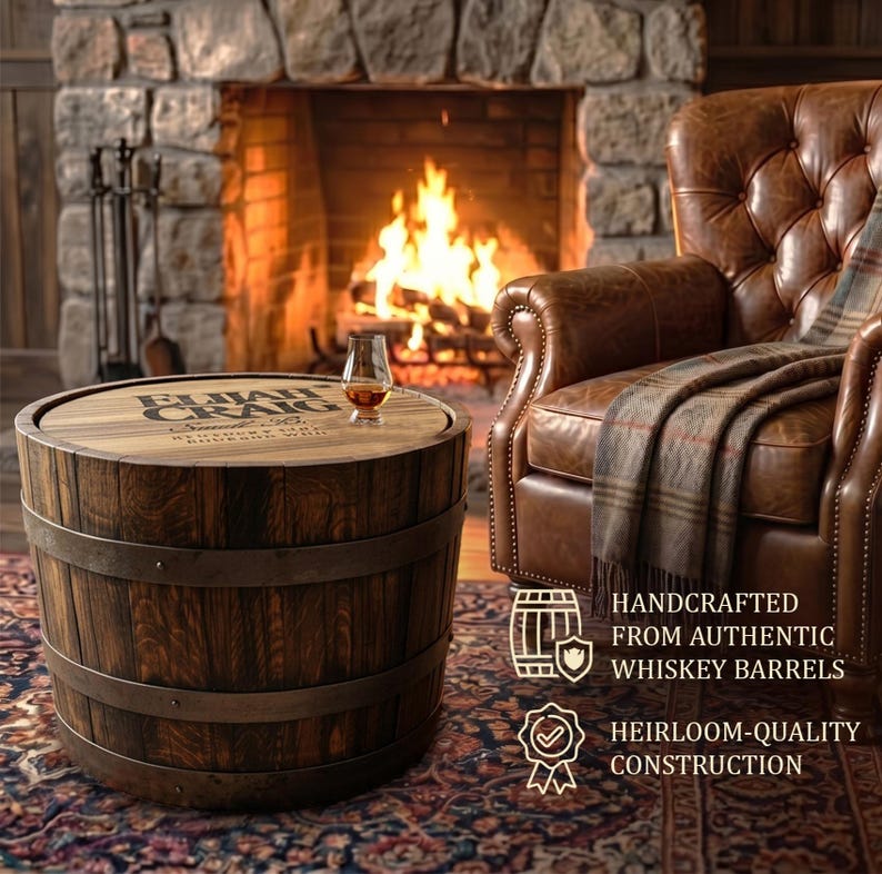 May include: A round wooden barrel table with metal bands, featuring the text "ELIJAH CRAIG" on the tabletop. A glass of amber liquid sits on top. The table is in front of a fireplace and a leather armchair.