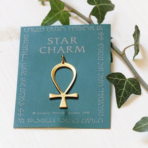 May include: A gold-coloured Ankh charm on a teal card with the text "STAR CHARM" and "Eastgate Resources London 1995".