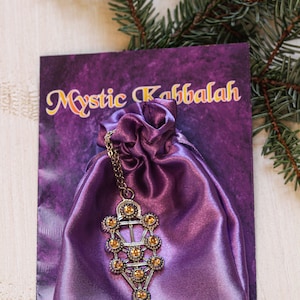 May include: A purple satin pouch with a silver Tree of Life pendant with amber-colored crystals. The pouch is on a card that says "Mystic Kabbalah".