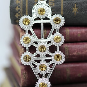 May include: A silver pendant necklace featuring a Tree of Life design with a geometric pattern and clear, faceted, amber-colored crystals.