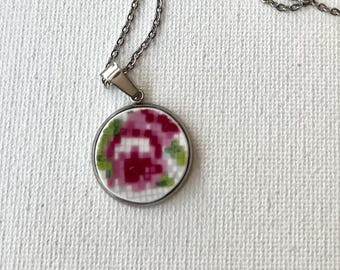Peut inclure: Un collier en chaîne argent avec un pendentif rond orné d'un motif floral rose et vert.