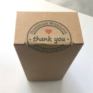 May include: A rectangular, brown cardboard box with a circular sticker on top. The sticker reads "HANDMADE WITH LOVE" around the edge, with "thank you" in the center, and a small red heart. The words "ESPECIALLY FOR YOU" are at the bottom of the sticker.