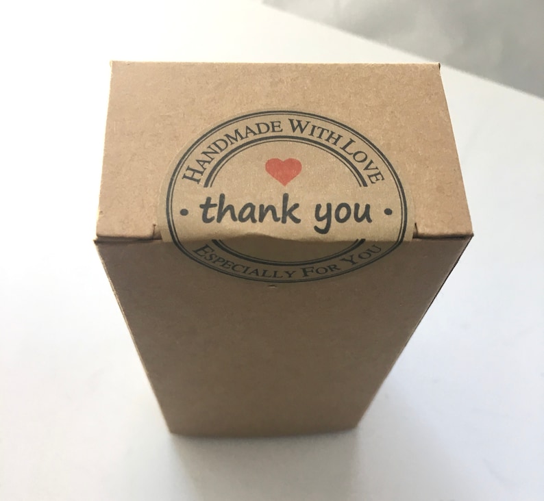 May include: A rectangular, brown cardboard box with a circular sticker on top. The sticker reads "HANDMADE WITH LOVE" around the edge, with "thank you" in the center, and a small red heart. The words "ESPECIALLY FOR YOU" are at the bottom of the sticker.