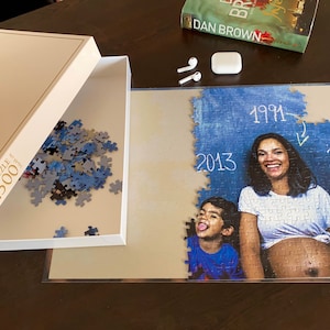 May include: A 500-piece jigsaw puzzle featuring a family portrait, partly put together. The image shows a woman and child with the years 1991, 2013, and 2018 written on the puzzle. The box is open, revealing blue and grey pieces.
