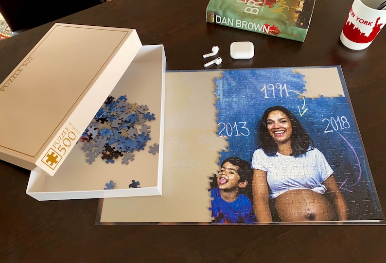 May include: A 500-piece jigsaw puzzle featuring a family portrait, partly put together. The image shows a woman and child with the years 1991, 2013, and 2018 written on the puzzle. The box is open, revealing blue and grey pieces.