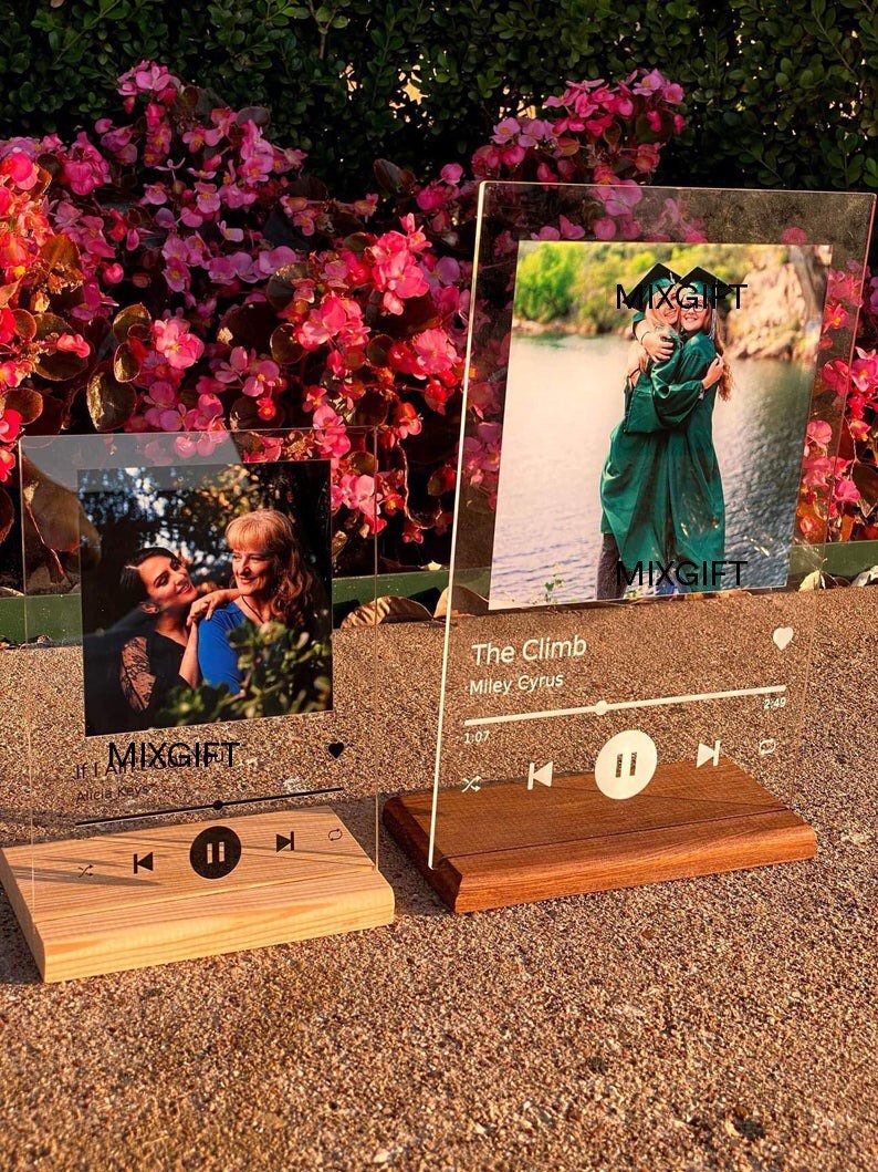 May include: Two clear acrylic photo frames with wooden bases. One frame displays a photo of two people, the other shows two people in graduation gowns. The text "MIXGIFT" is visible on both frames. The second frame has the text "The Climb" and "Miley Cyrus".