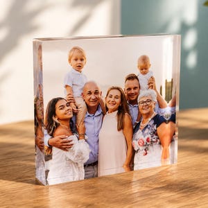 Può includere: Un blocco acrilico trasparente, spesso e rettangolare, che presenta una fotografia a colori stampata di un gruppo familiare multigenerazionale. L'immagine mostra sette persone, inclusi due bambini piccoli, in posa insieme all'aperto.