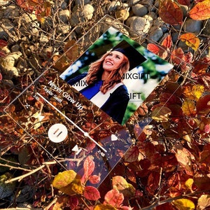 May include: A clear acrylic plaque featuring a photo of a woman in a graduation cap and gown. The plaque has a music player interface design with the song title "Never Grow Up" by Taylor Swift. The background includes colorful autumn leaves.