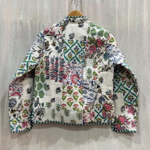 Pu&ograve; includere: Una giacca trapuntata bianca con stampa floreale. La giacca ha un colletto alla coreana e maniche lunghe. Il tessuto &egrave; un patchwork di diversi motivi floreali in tonalit&agrave; di rosa, verde e blu.
