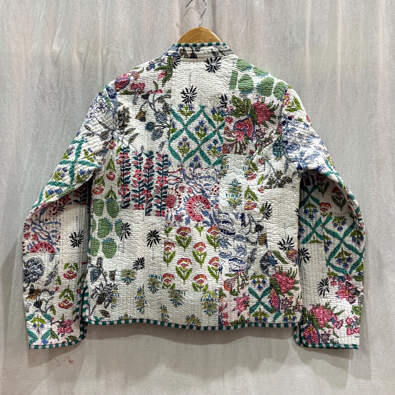 Pu&ograve; includere: Una giacca trapuntata bianca con stampa floreale. La giacca ha un colletto alla coreana e maniche lunghe. Il tessuto &egrave; un patchwork di diversi motivi floreali in tonalit&agrave; di rosa, verde e blu.