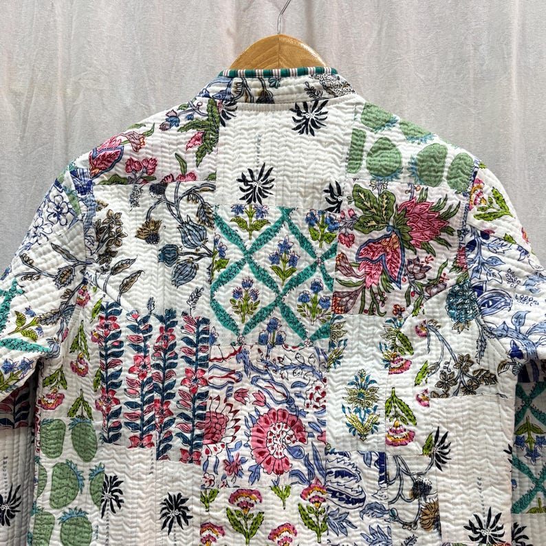 Pu&ograve; includere: Una giacca trapuntata bianca con un design a patchwork che presenta motivi floreali e geometrici in tonalit&agrave; di verde, blu, rosa e nero.
