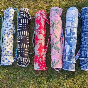 May include: Seven colorful yoga mat carriers with various patterns, including floral, geometric, and animal prints. The carriers are rolled up and have straps for easy carrying. The colors include green, blue, black, red, pink, and white.