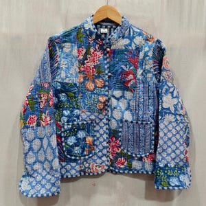 May include: A quilted jacket with a vibrant floral pattern in shades of blue, pink, and orange. The jacket features a mandarin collar, two front pockets, and a button-up closure. The design incorporates various fabric patterns.