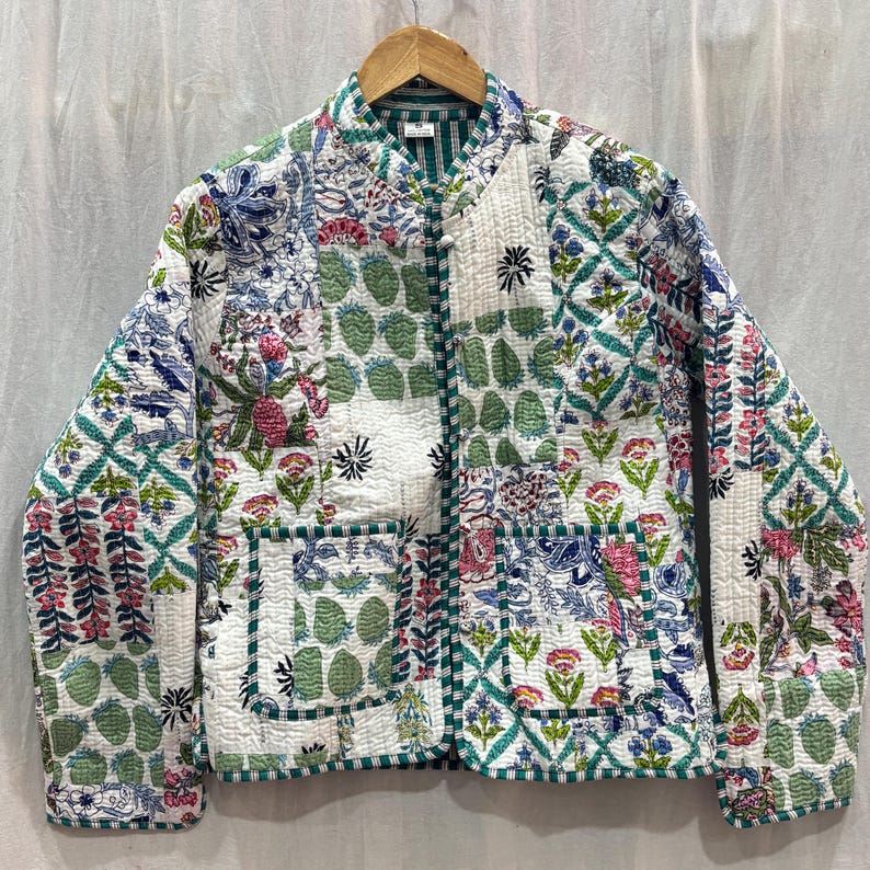 Pu&ograve; includere: Una giacca trapuntata bianca con stampa floreale verde. La giacca ha un colletto alla coreana e una chiusura con cerniera. Presenta due tasche a toppa sul davanti.
