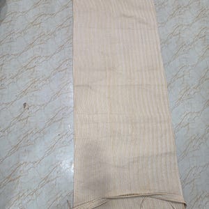 May include: A rectangular fabric runner featuring a fine vertical pinstripe pattern in mustard yellow and white. The textile has finished edges and includes thin fabric ties at the bottom corners for securing the piece in place during use.