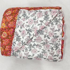 May include: Folded floral quilt featuring a vibrant mix of colors. One side showcases a pattern of red, orange, and yellow flowers, while the other displays a white background with pink roses and gray leaves. A cozy bedding item.