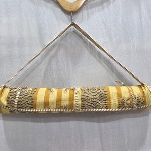 May include: A rolled fabric mat featuring a repeating pattern of yellow and white vertical stripes interspersed with sections of dark tiger-print motifs. The mat is secured with a matching striped fabric strap and hangs from a wooden hanger.