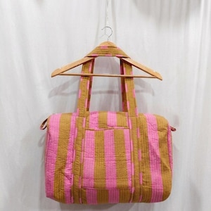 May include: A rectangular quilted duffel bag featuring vertical stripes in mustard yellow and bright pink. The bag includes two sturdy fabric handles attached to the top, a zippered main compartment, and a visible exterior pocket on the front side.