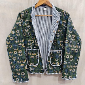 Könnte beinhalten: Eine grüne Steppjacke mit blau-gelbem Blumenmuster. Die Jacke hat ein gestreiftes Futter und Zierleisten, zwei Vordertaschen und Holzknöpfe. Die Jacke hängt an einem Holzkleiderbügel.