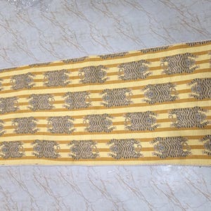 May include: A rectangular textile runner featuring a repeating pattern of black tiger motifs arranged in horizontal rows against a background of alternating mustard yellow and light cream stripes, finished with a simple stitched edge border.
