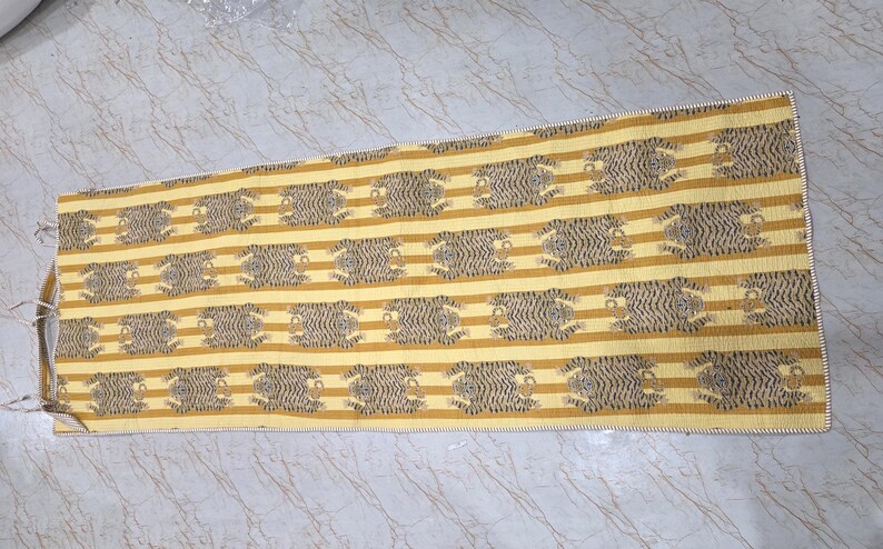 May include: A rectangular textile runner featuring a repeating pattern of black tiger motifs arranged in horizontal rows against a background of alternating mustard yellow and light cream stripes, finished with a simple stitched edge border.