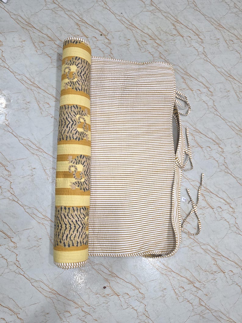 May include: A quilted fabric roll featuring a yellow and white striped pattern with a repeating dark gray tiger print on one side and a fine white and yellow pinstripe pattern on the other, complete with thin fabric ties for securing the roll.