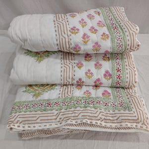 May include: A white cotton quilt with a floral print in shades of pink, green, and brown. The quilt is folded in thirds, showing the different patterns on each side.