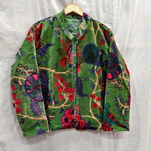 Könnte beinhalten: Grüne Samtjacke mit einem lebendigen Blumenmuster in Rot, Blau und Pink. Die Jacke hat einen Stehkragen und einen Knopfverschluss. Das Design umfasst stilisierte Blumen, Blätter und Vögel.