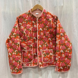 Könnte beinhalten: Eine rote gesteppte Jacke mit Blumendruck und weißem Besatz. Die Jacke hat einen Stehkragen, einen Knopfverschluss und zwei aufgesetzte Taschen.