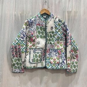 Pu&ograve; includere: Una giacca trapuntata bianca con un design a patchwork che presenta motivi floreali e geometrici in tonalit&agrave; di verde, blu e rosa. La giacca ha una chiusura con cerniera e due tasche a toppa.