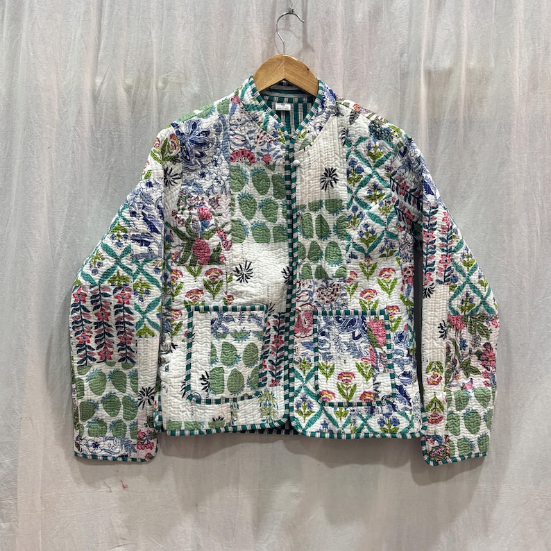 Pu&ograve; includere: Una giacca trapuntata bianca con un design a patchwork che presenta motivi floreali e geometrici in tonalit&agrave; di verde, blu e rosa. La giacca ha una chiusura con cerniera e due tasche a toppa.