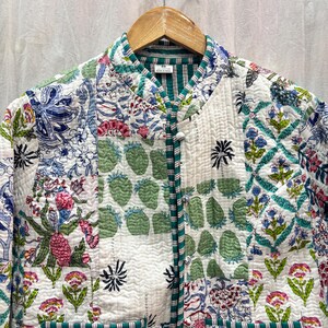 Pu&ograve; includere: Una giacca trapuntata bianca con un design a patchwork che presenta motivi floreali e geometrici in tonalit&agrave; di verde, blu, rosa e rosso. La giacca ha un colletto alla coreana e una chiusura con bottoni.
