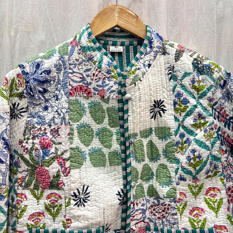 Pu&ograve; includere: Una giacca trapuntata bianca con un design a patchwork che presenta motivi floreali e geometrici in tonalit&agrave; di verde, blu, rosa e rosso. La giacca ha un colletto alla coreana e una chiusura con bottoni.