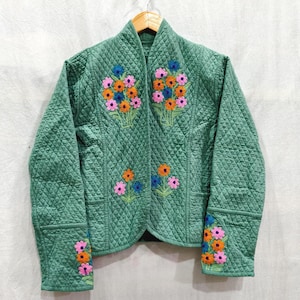 May include: A sage green quilted jacket featuring a diamond-stitched pattern and embroidered floral bouquets in shades of pink, orange, and blue. The jacket has a stand-up collar, long sleeves, and an open front design with floral accents.