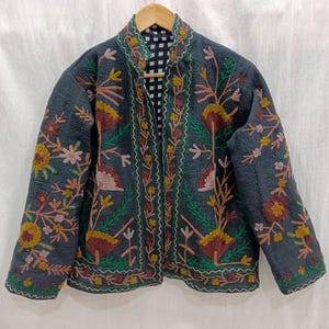 May include: A dark blue jacket with intricate floral embroidery in shades of green, pink, and brown. The jacket has a mandarin collar and a black and white checkered lining.