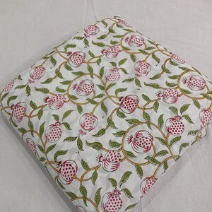 May include: A folded piece of white fabric featuring a repeating pattern of pink pomegranates with green leaves and yellow vines. The textile displays a block-printed style design with consistent spacing between the botanical motifs across the surface.